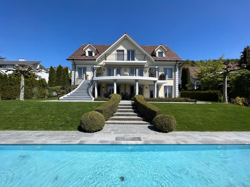 Large villa, brown roof, white walls, large windows, balcony, swimming pool, well-maintained garden, stairs leading to the entrance