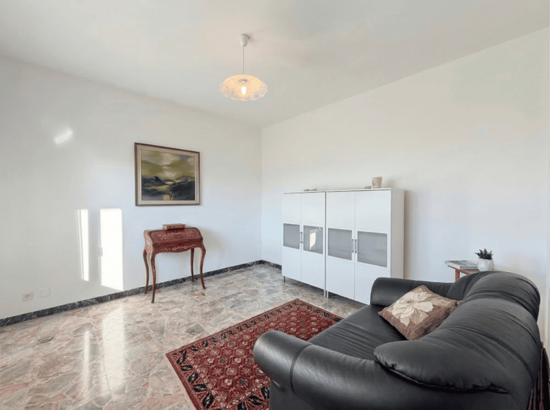 Living room with white walls, black leather sofa, wooden table, white cabinet, picture frame, rug, pendant light