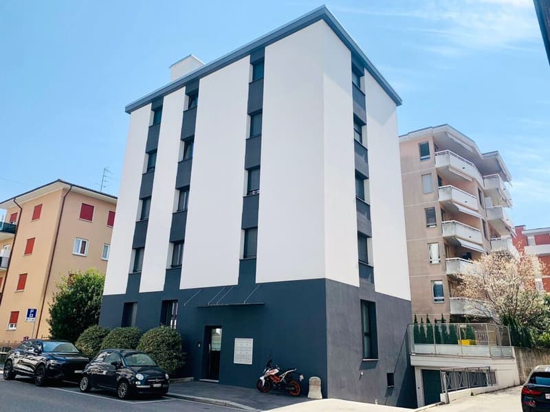 Modern apartment building with white and blue walls, multiple windows, and a motorcycle parked in front.