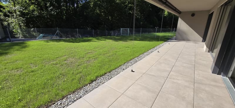 tiled patio, grassy lawn, gravel border, chain link fence, trees