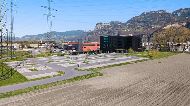Aerial view of the construction site with buildings and parking lot. Located next to mountains.