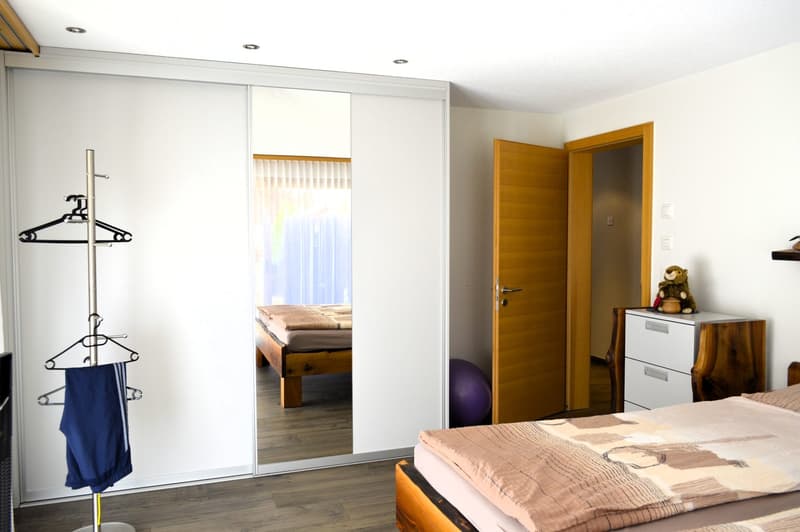 Bedroom with wooden bed, bed cover, white wardrobe, closet with hangers, fitness ball.