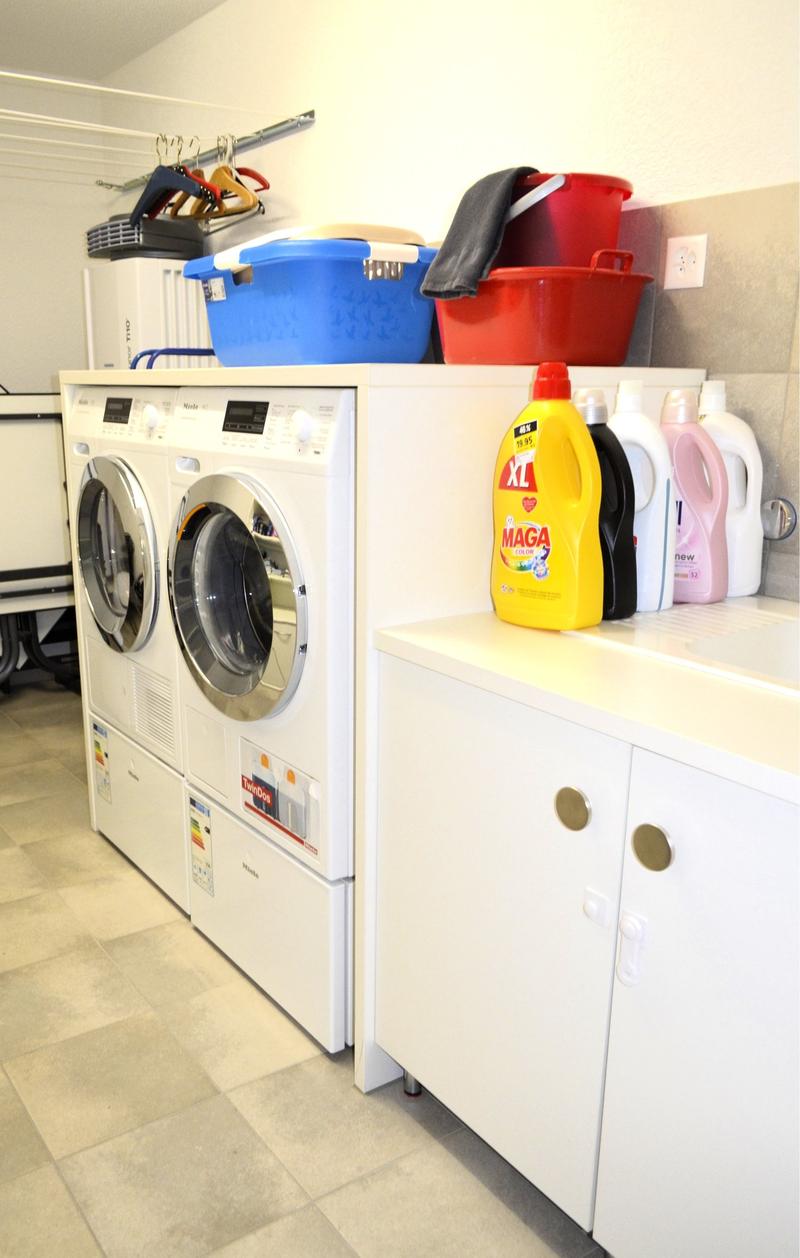 Modern laundry room with two washing machines, a cabinet, shelves, and storage boxes