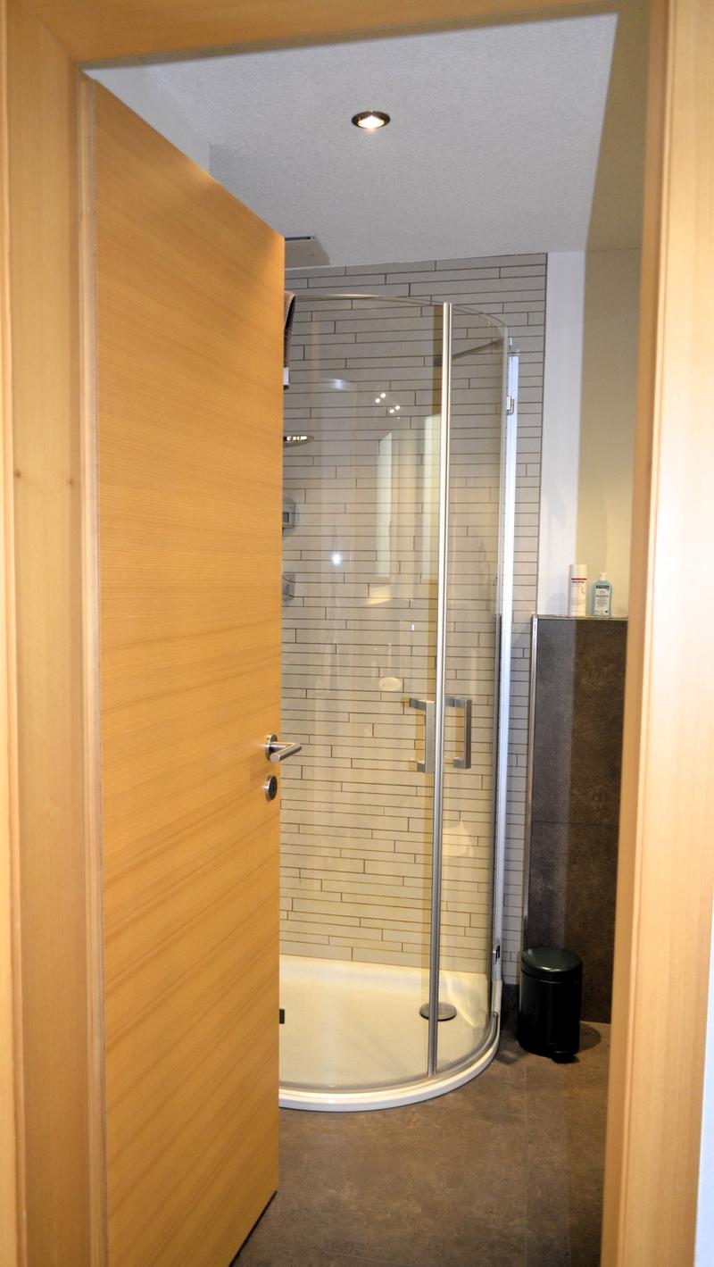 Modern shower room with walk-in shower, tiled wall, and wooden door