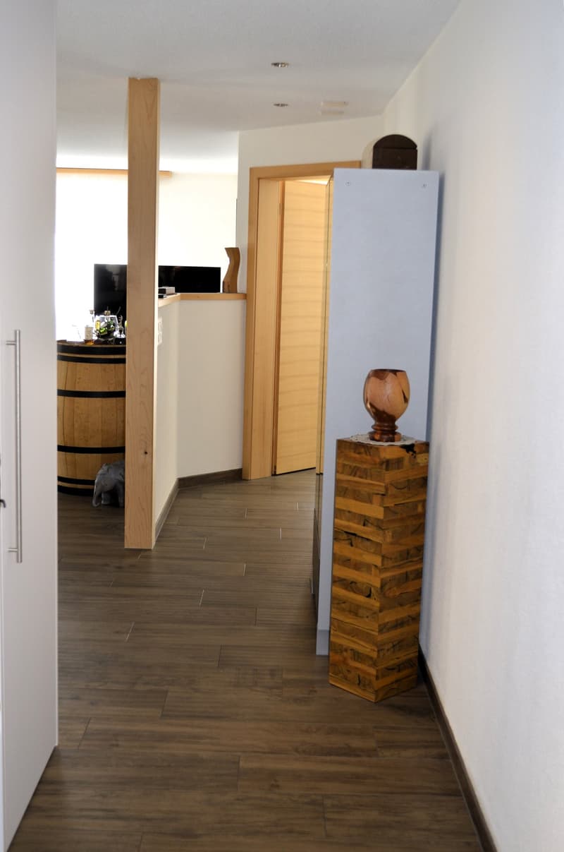 Dark wooden floor, white walls, hardwood column, light wooden door, barrel in the distance, modern wooden structure