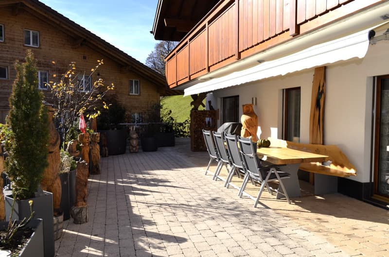 Brick walled houses, balcony with wooden table and chairs, small statue, wood carving, outdoor bench, and potted plants