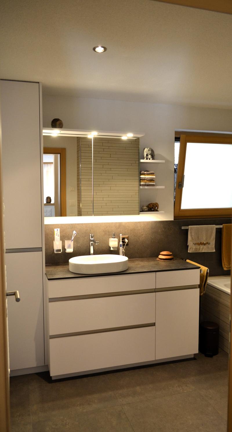 Bathroom with sink, mirror, shelves, bathtub, towel rack, tiled floor, white cabinets, and wooden door.