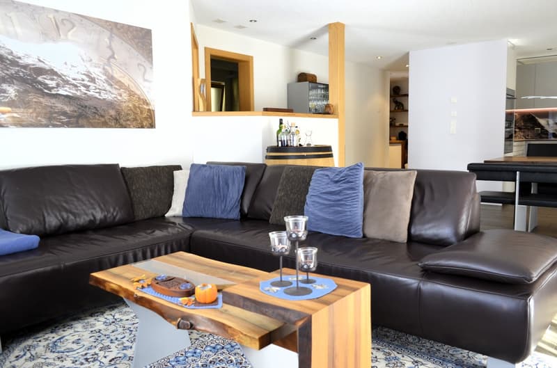Black leather couch with pillows, wooden coffee table, table lamps, decorative items, carpet, and a large wall art.