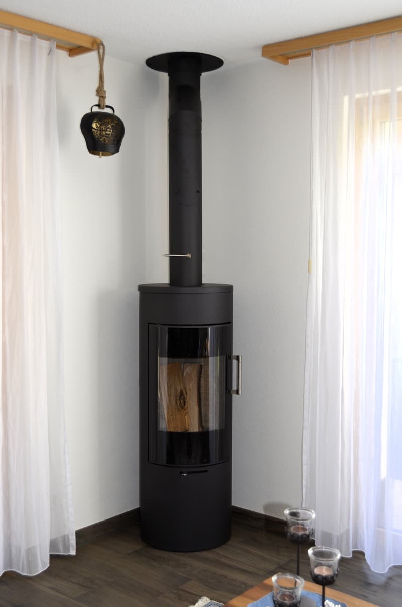 A modern black fireplace in the corner of a room, wood flooring, white curtains