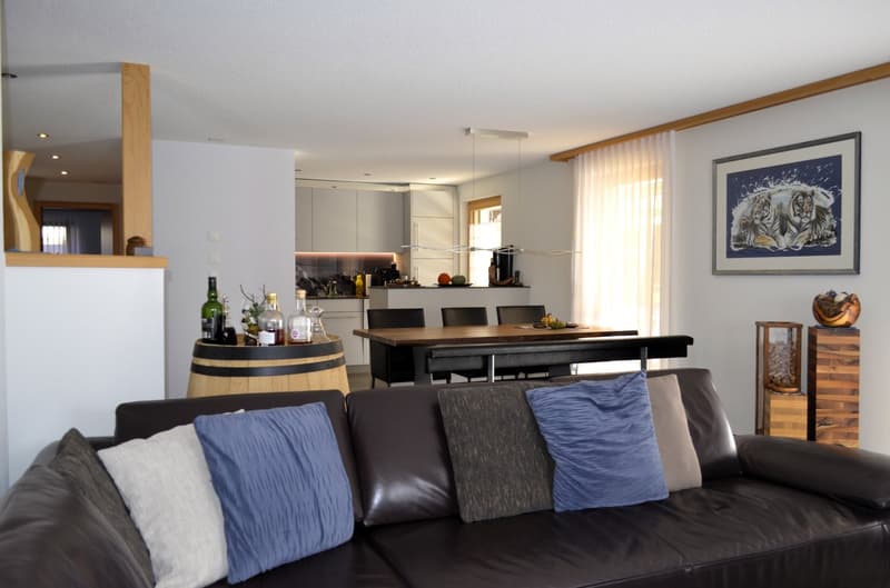 modern interior, black leather couch, wooden barrel as table, dining table with chairs, kitchen with island, wine bottles, painting