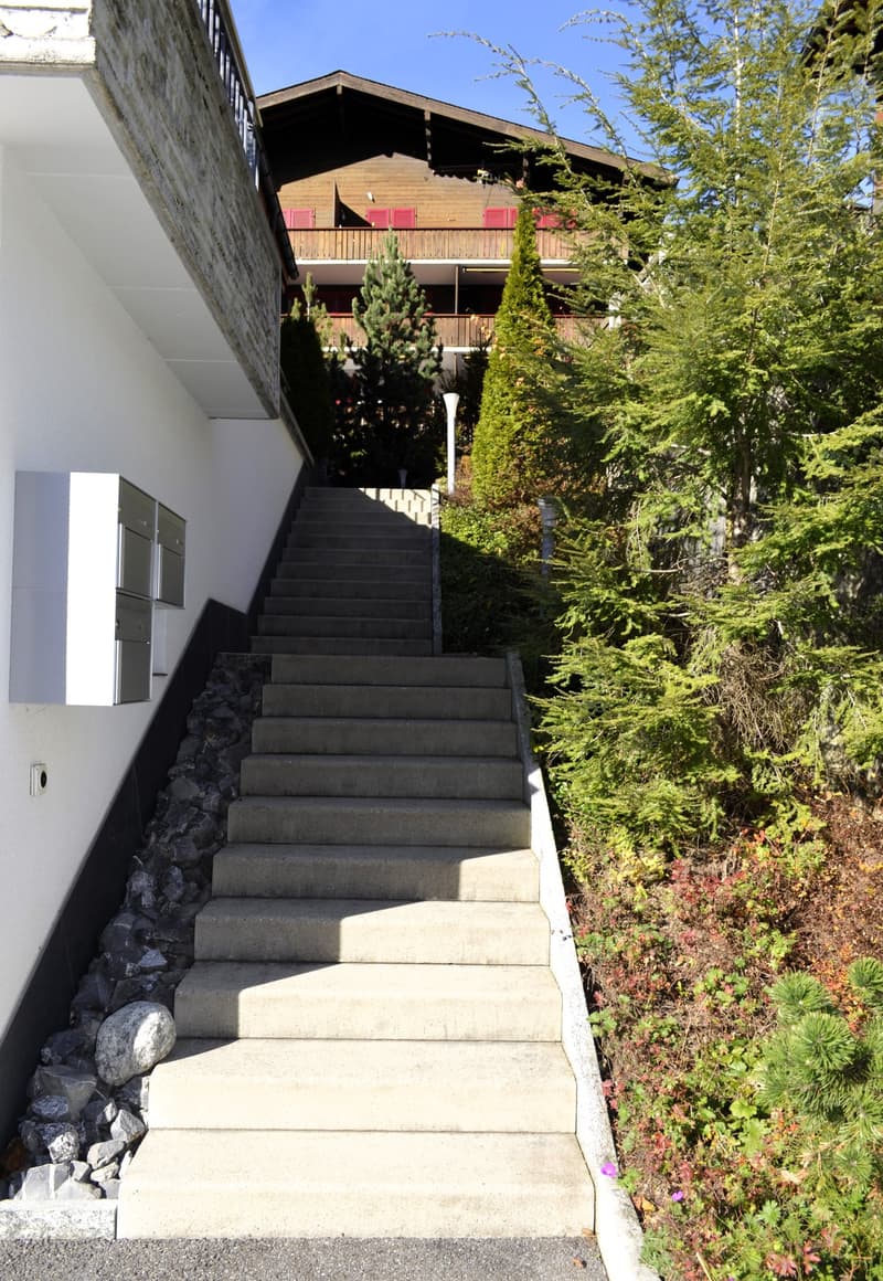 concrete steps leading to a balcony above ground level, letter boxes, bushes, large trees