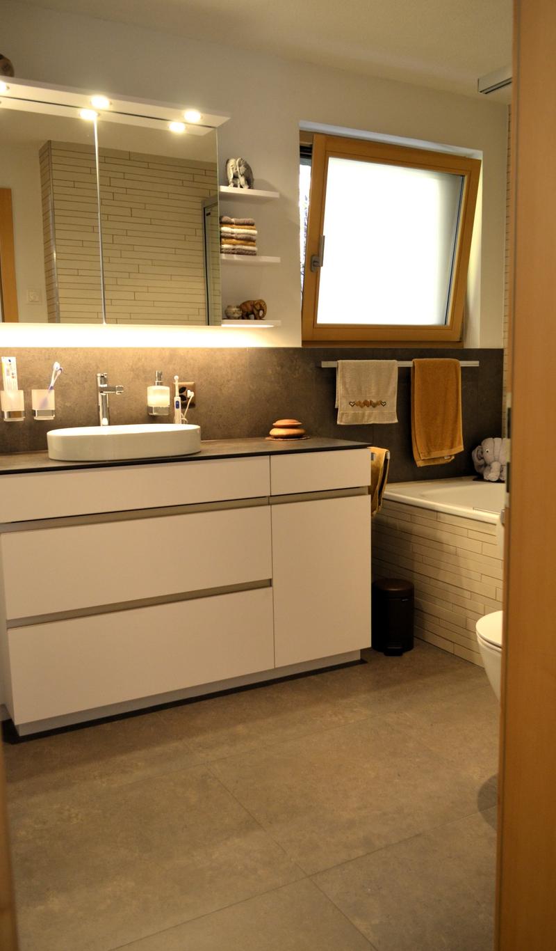 white sink, modern cabinet, white ceramic tile, open door to bathtub, large mirror, shelves, and elephant sculptures