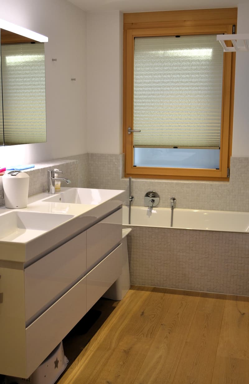 Bathroom with double sink, bathtub, window, mirror, and wooden floor