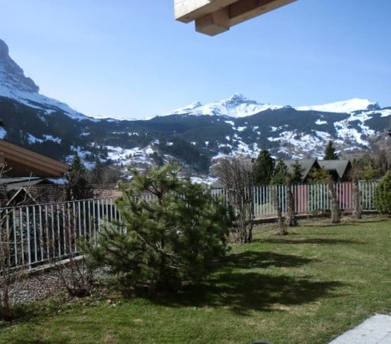fenced garden with green grass, small trees, and a view of the mountains