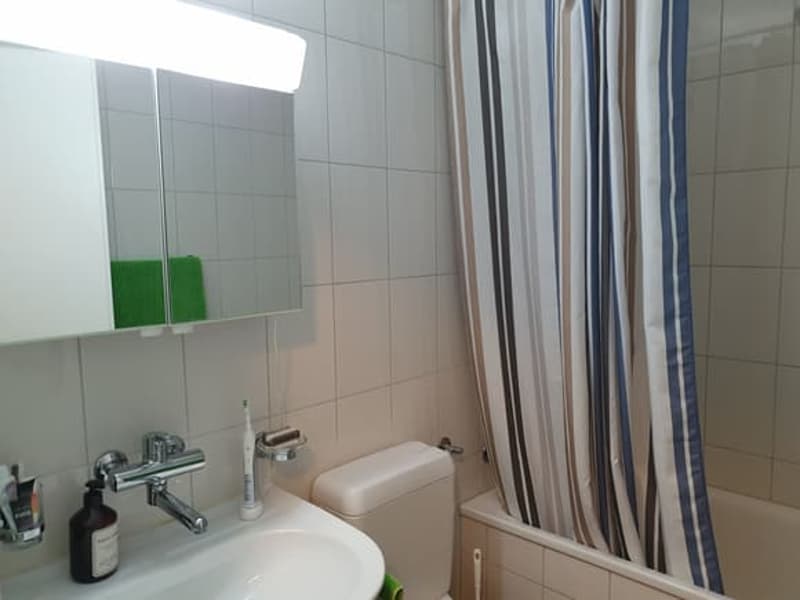 A clean bathroom with a sink, toilet, bathtub, shower curtain, mirror, and towel