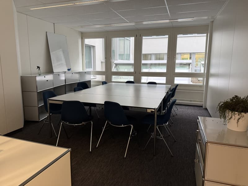 A conference room with a long table, chairs, a whiteboard, and a cabinet with a bottle on top.