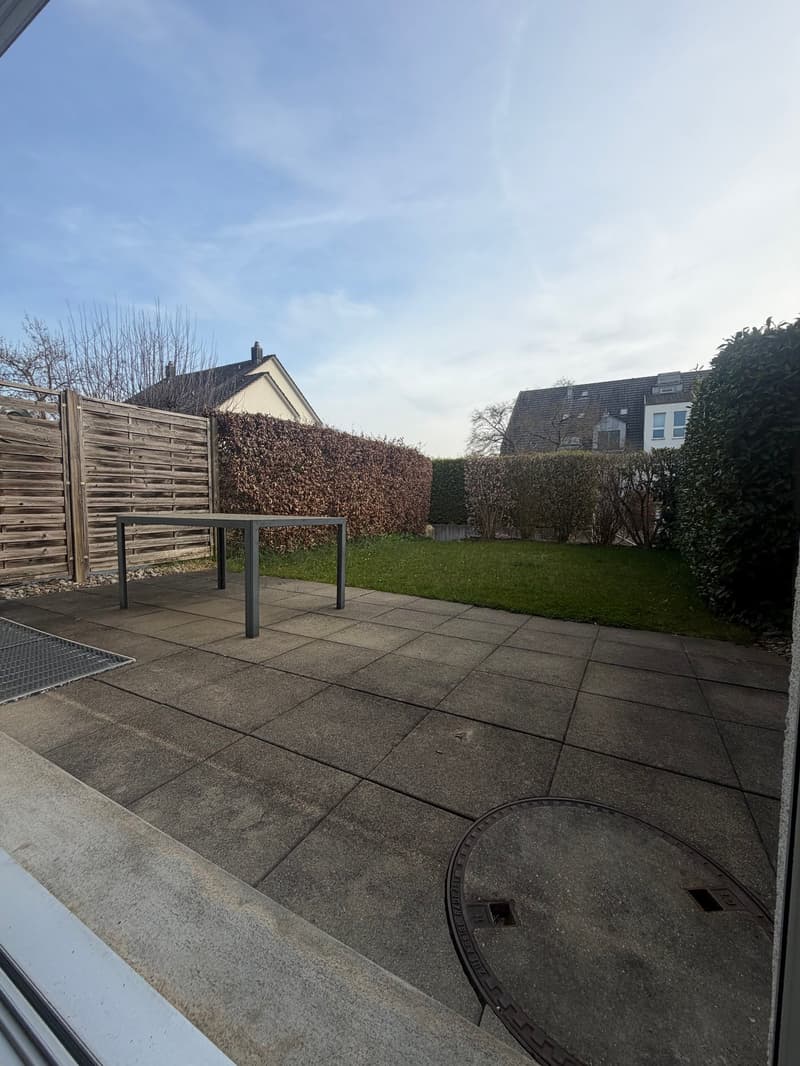 Rectangular paved terrace, table, hedge, and manhole