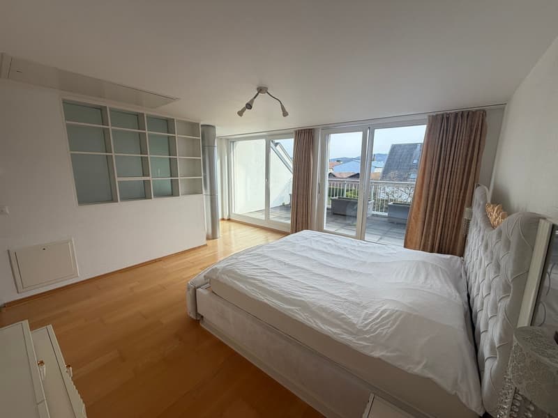 modern bedroom with double bed, white walls, wooden floor, large sliding glass doors, balcony with outdoor furniture, nightstands, wardrobe, ceiling lamp
