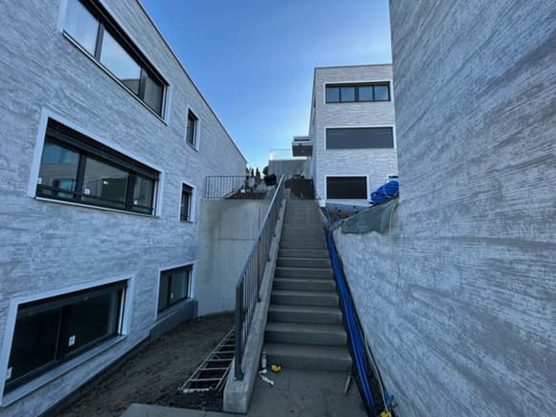 modern building with concrete walls, large windows, stairs leading to upper floor, metal handrail