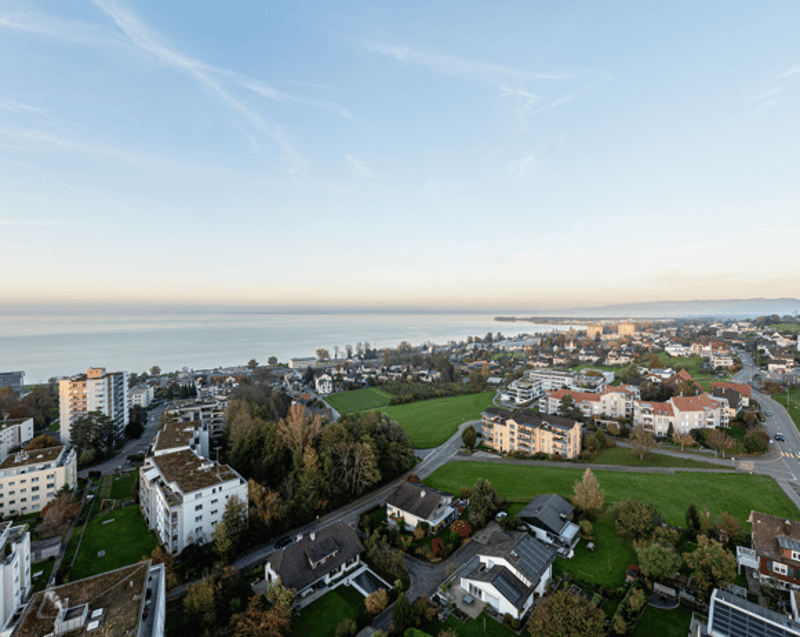 Aerial view of a neighborhood with buildings, green spaces, and a body of water in the distance