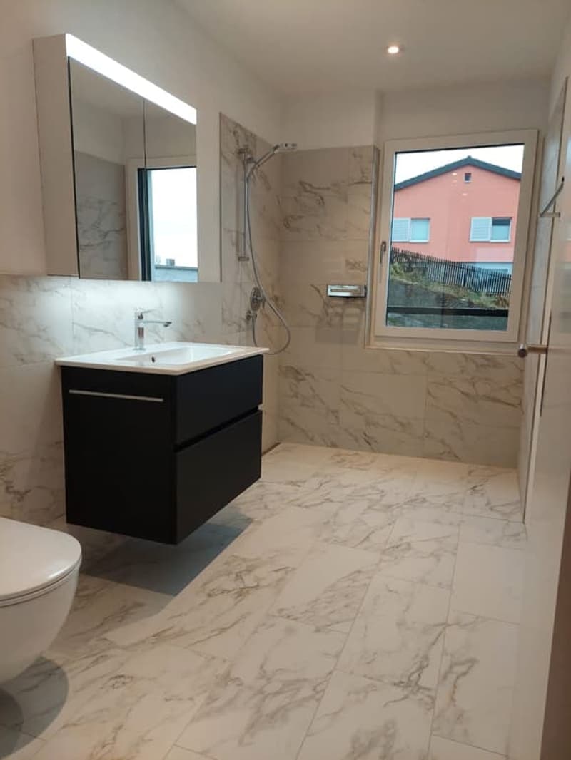 Bathroom with white marble tiles, black cabinet, white sink, shower, toilet, mirror, window
