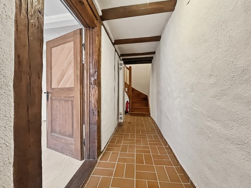 corridor with brown tiled floor, wooden door, wall-mounted radiator, staircase leading up