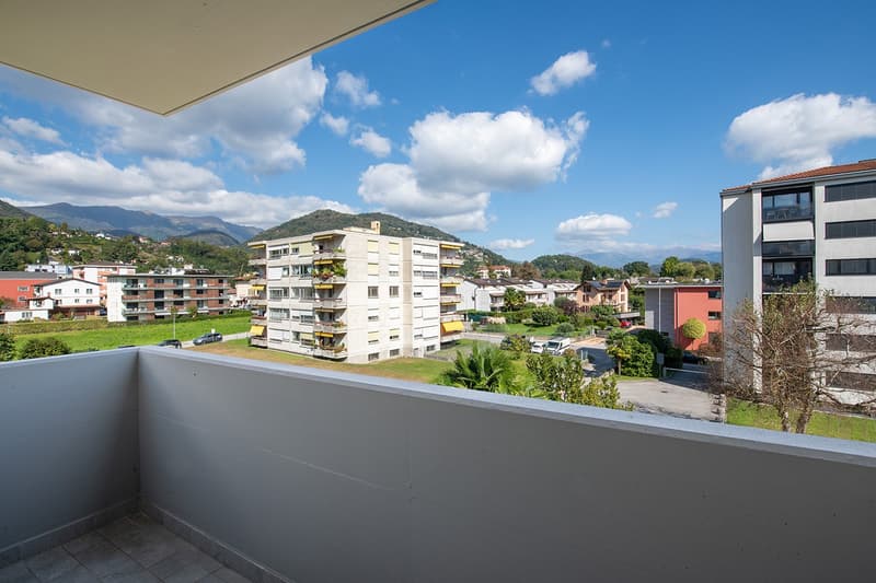 Balcony with tiled floor, overlooking a cityscape with buildings, mountains, and greenery