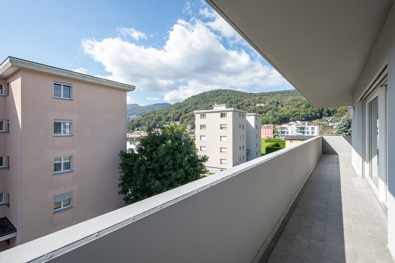 Balcony with tiled floor, white walls, and a view of the mountains and buildings