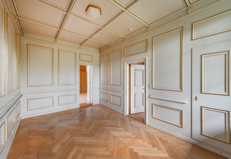 empty room, wooden parquet floor, white walls, gold trims, two doors, one leading to another room