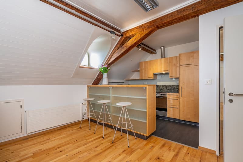 kitchen with wooden floor, wooden cabinets, glass bar counter, white stools, white walls, arched window, vase with flowers, radiator