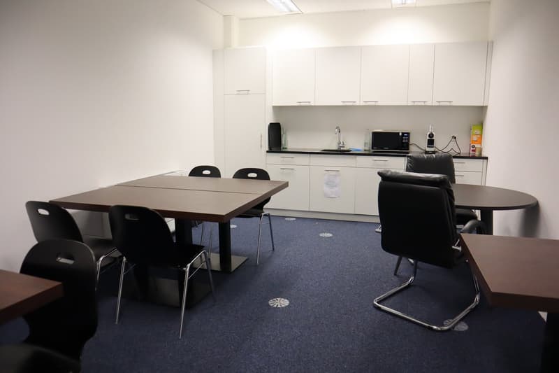 empty room with tables and chairs, white cabinets, microwave, sink, blue carpet