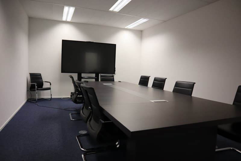 empty conference room with a large table, black chairs, a flat screen TV, and white walls