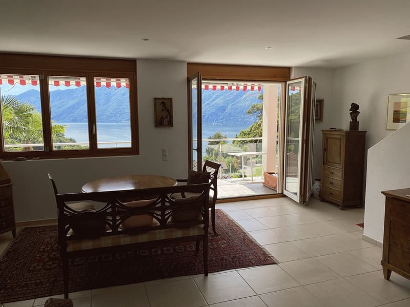 living room with balcony, large windows, wooden table, chairs, rug, wooden cabinet, picture frames, statue, tiled floor