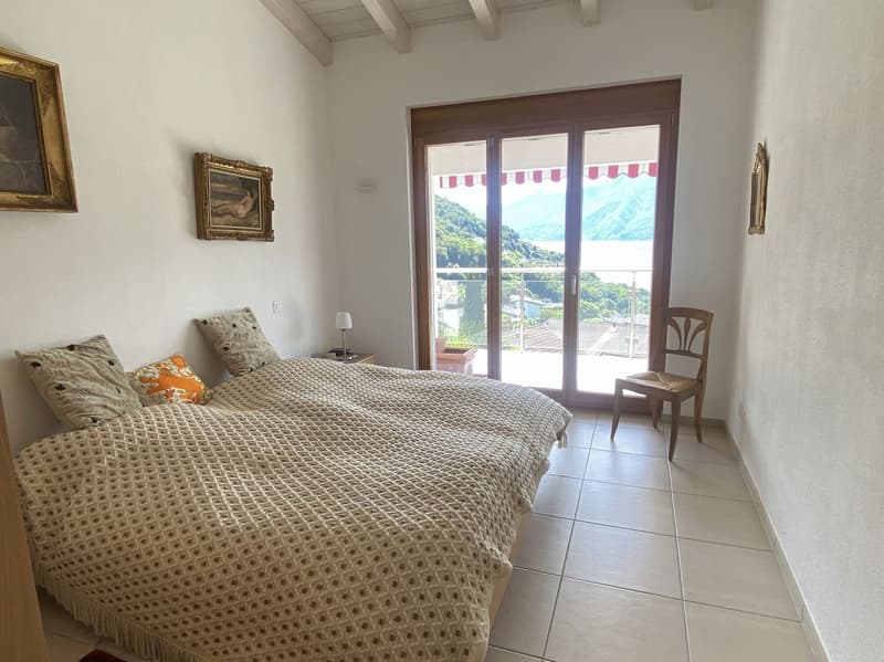 double bed, two pillows, bedside table with lamp, wooden chair, sliding glass door to balcony, framed pictures on wall