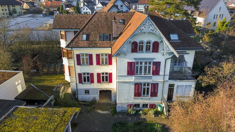 white painted house, red shutters, multiple balconies, large roof, green rooftop, brick floor