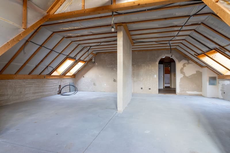 attic room with beams, concrete floor, unfinished walls, electrical wires, windows, pillar