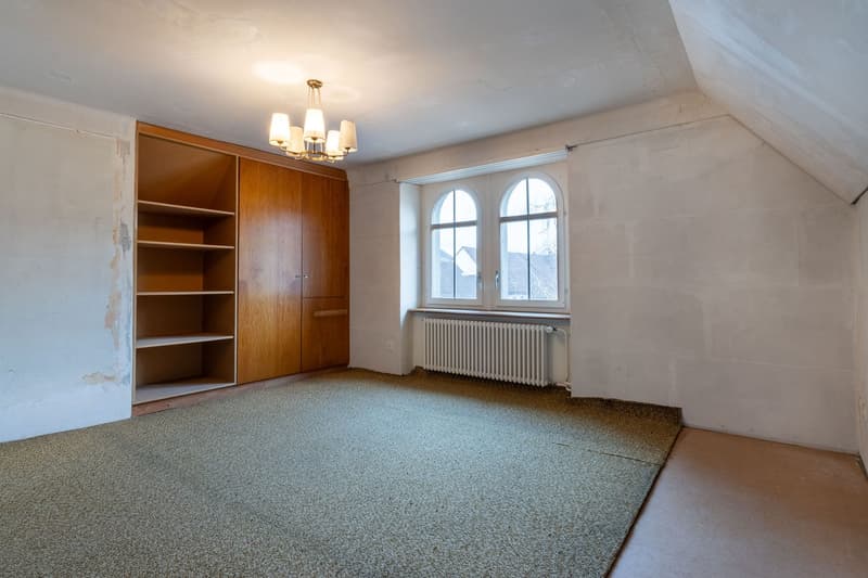 Empty room with a carpet, large window, a built-in wooden cabinet, a ceiling lamp, and a radiator