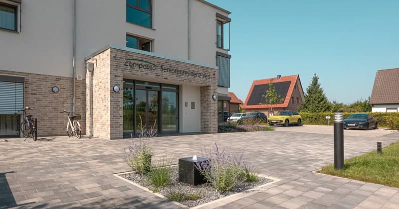 Modern apartment building, brick facade, glass entrance doors, parking area, bicycles parked, solar panels on roofs