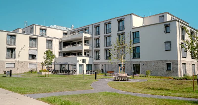 Modern apartment building, white exterior, multiple balconies, brick accents, landscaped garden, outdoor seating area, paved pathways