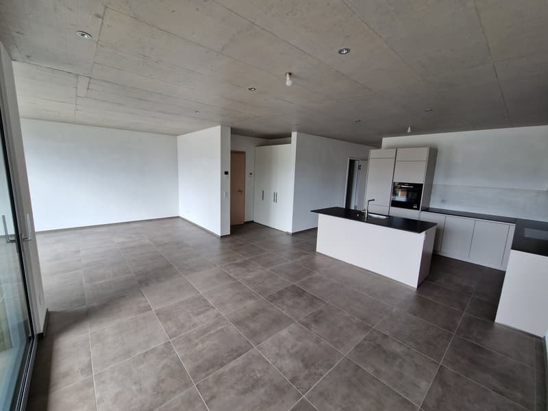 Empty room with white walls, gray tiled floor, kitchen island with black countertop, white cabinets, and a sink with a faucet.