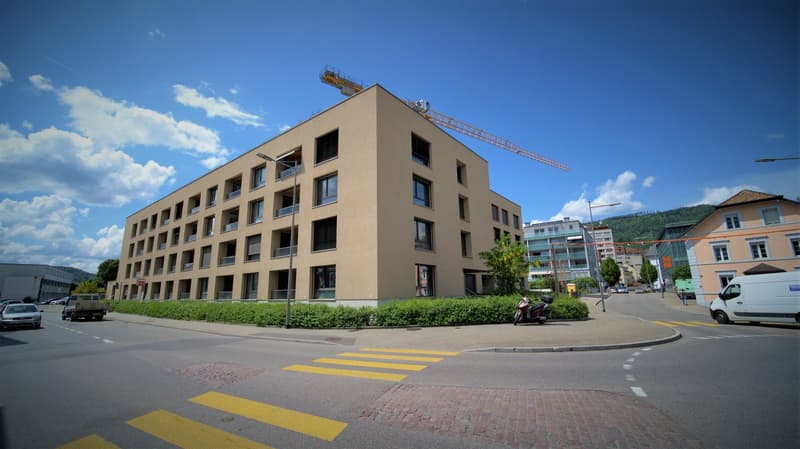 5 story building, beige exterior, multiple balconies, street view, construction crane on top