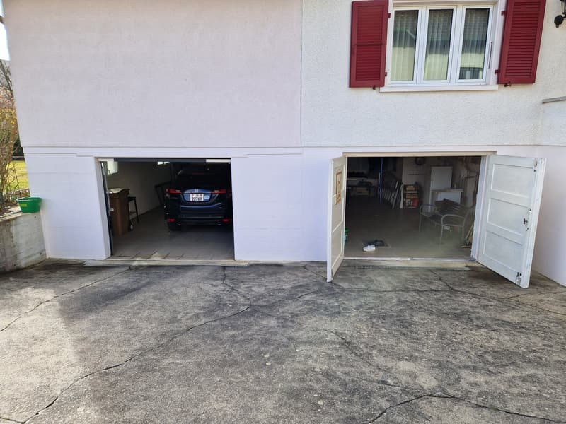 white house with red shutters, two garages, one with a car parked inside