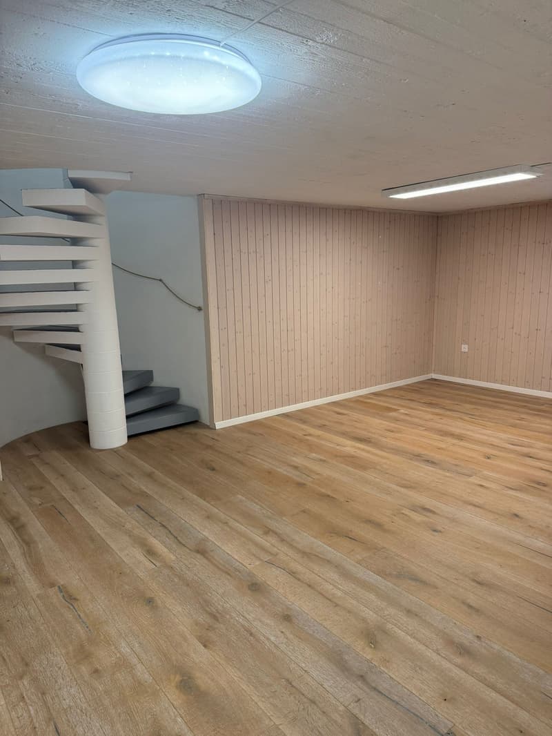Empty room with wooden floor, spiral staircase, wooden wall paneling, ceiling lights