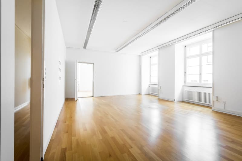 Empty room with wooden floors, white walls, and three windows.