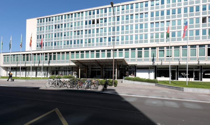 Modern office building with multiple floors, glass windows, entrance with awning, flags on poles, bicycles parked in front, street light, and a person walking.