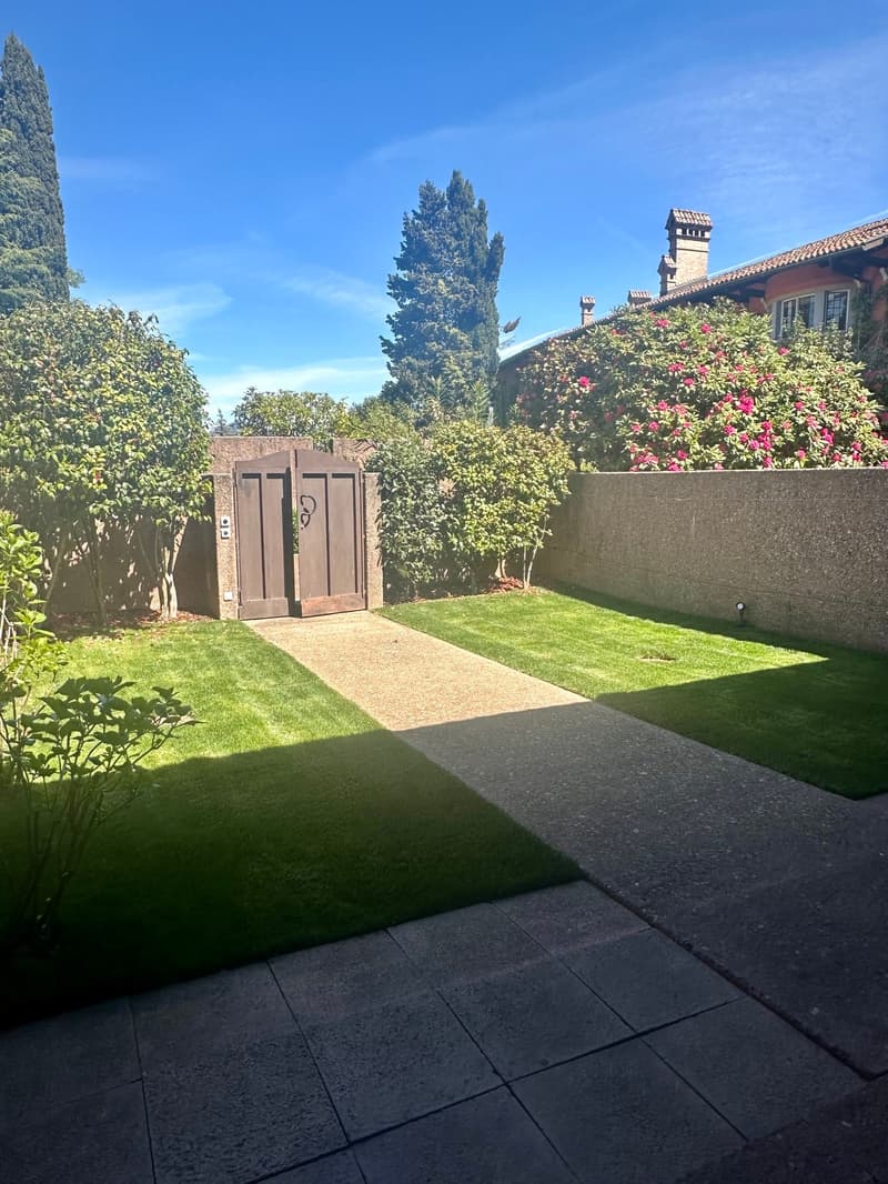 well-maintained garden with a paved walkway, lush green grass, and a wooden gate leading to the entrance