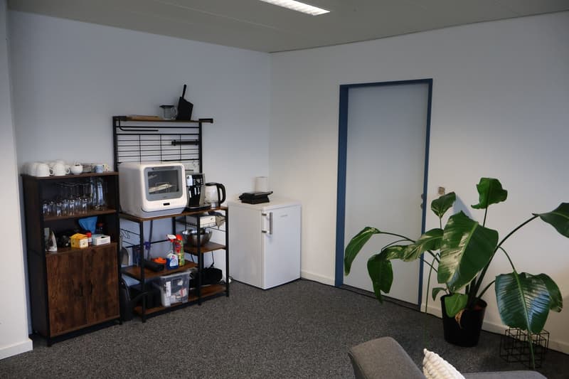 small room with a shelf, a mini fridge, a microwave, a coffee machine, a plant, and a couch
