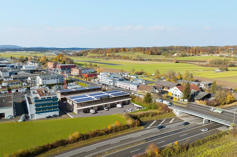 Industrial building with solar panels on the roof, multiple buildings in the area, parking lot, highway