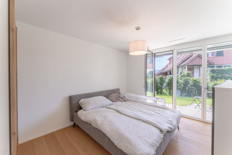 bedroom with bed, pillow, blanket, lamp, sliding glass doors, wooden floor, white walls, view of garden