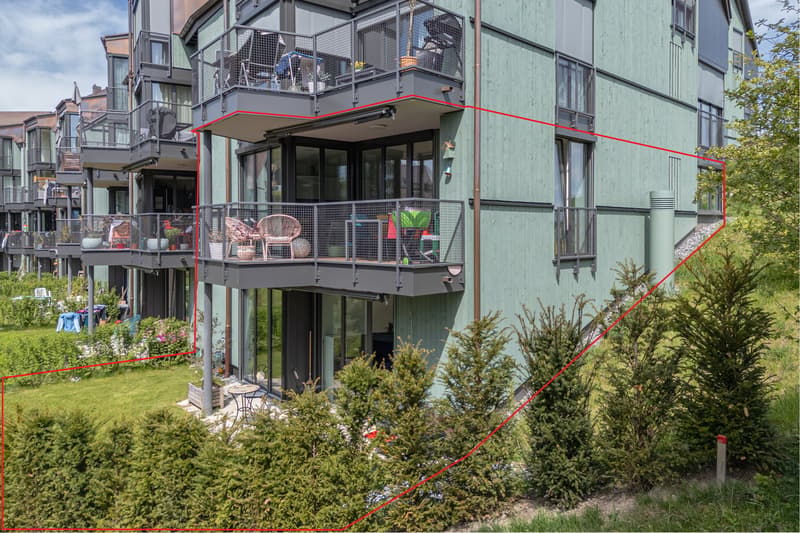Modern apartment building with multiple balconies, green exterior, large windows, and a sloped terrain.